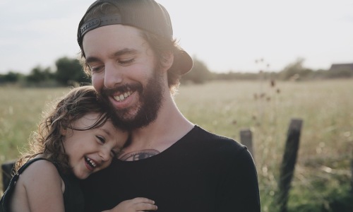 smiling little girl rests her head on her father's chest in front of an open field